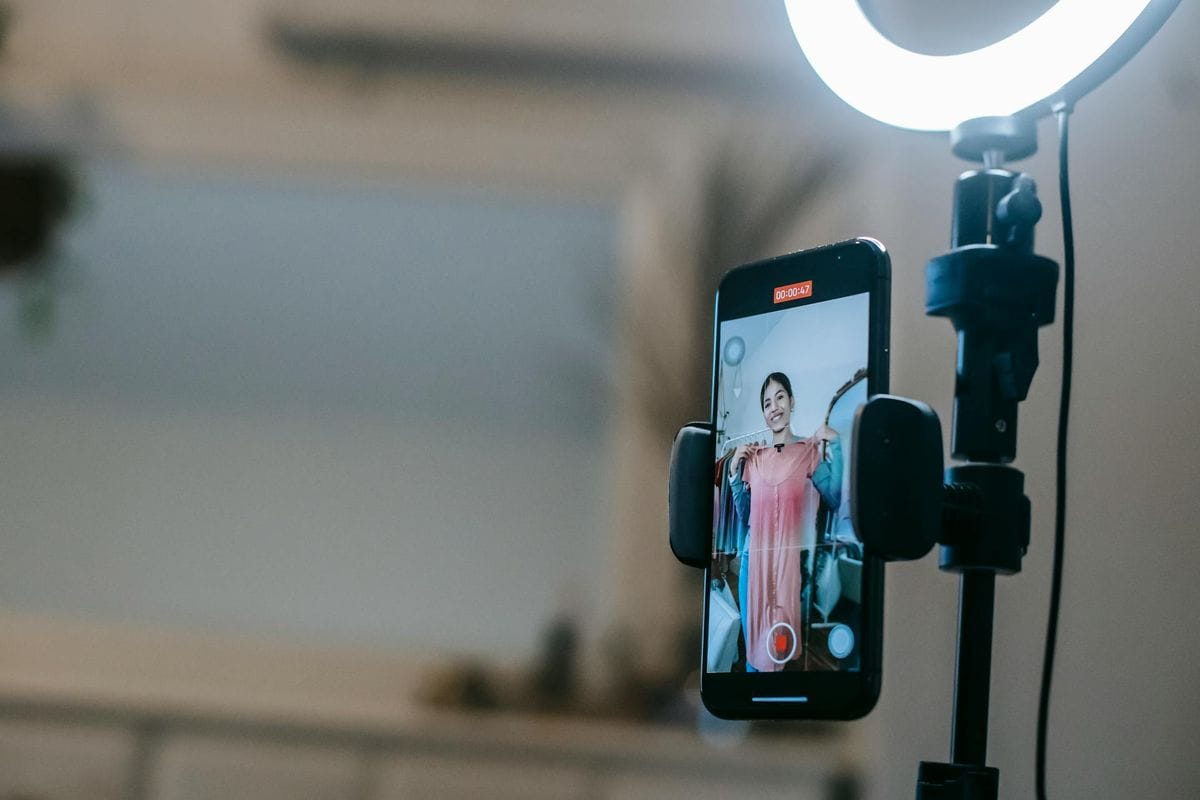A woman livestreaming with a smartphone and ring light in a modern home setting.
