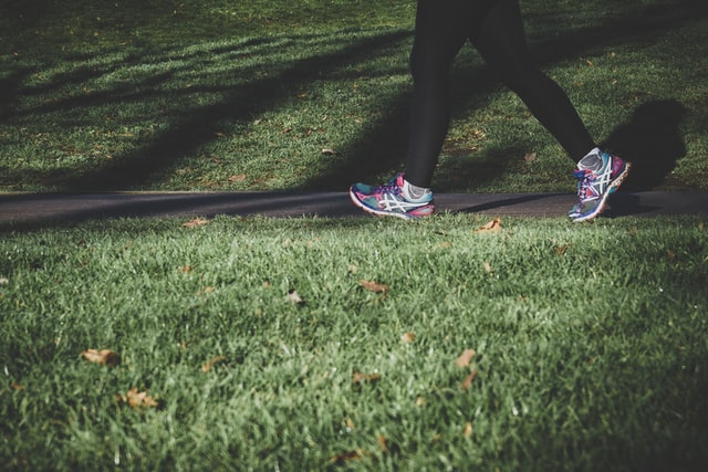 Legs wearing running shoes, walking on a path through a park