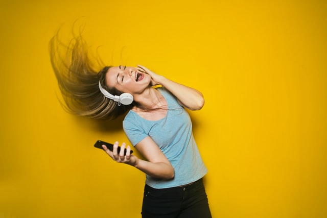 Women wearing noise cancelling headphones and holding a mobile singing loudly.