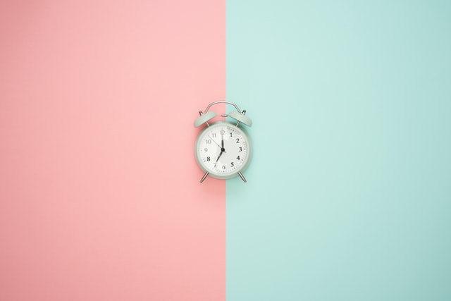 A white alarm clock against a pink and light green background