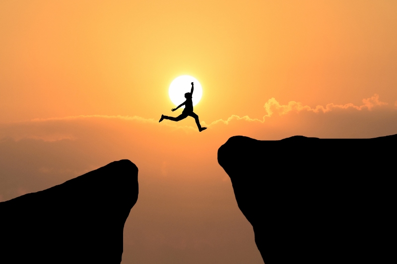 a man jumping from a mountain to another