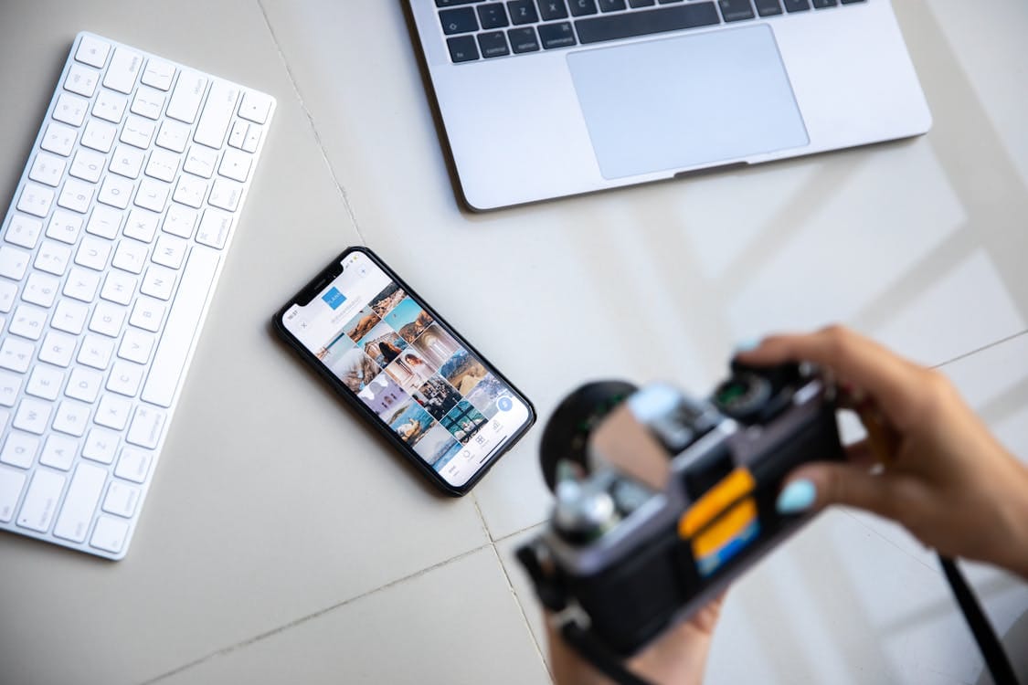 Free Person using vintage camera with smartphone and laptop in creative setup. Stock Photo