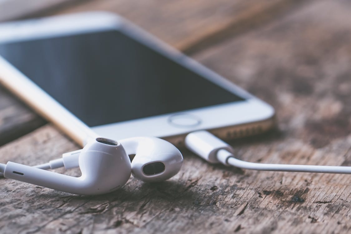 Free A close-up image of a smartphone and earphones lying on a wooden surface, capturing a moment of connectivity and technology. Stock Photo