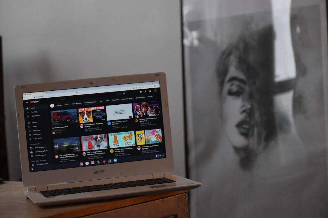 Free A cozy indoor setting with an Acer laptop displaying YouTube on a wooden table beside artwork. Stock Photo