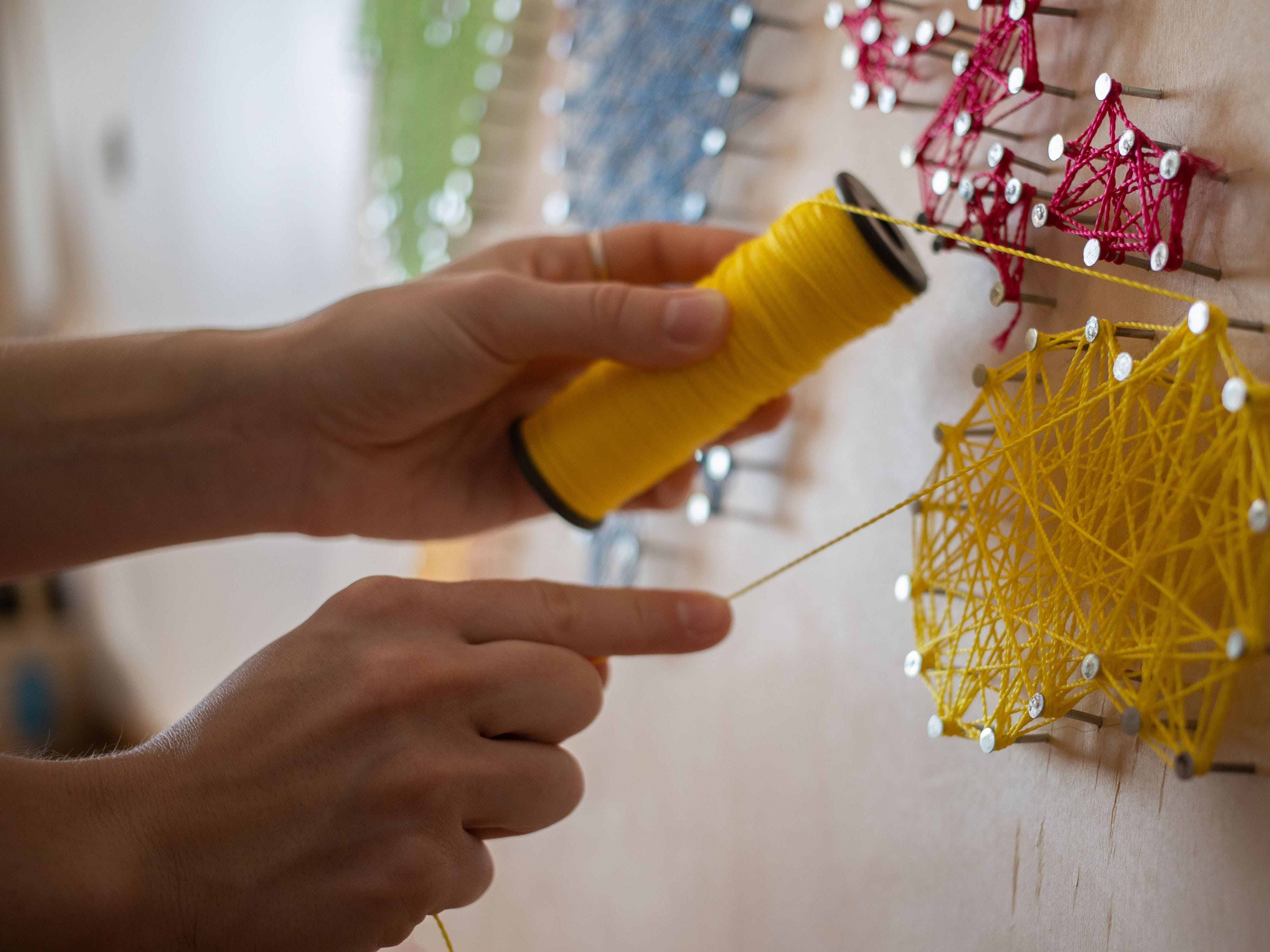 Hand creating yellow string art on a wooden board
