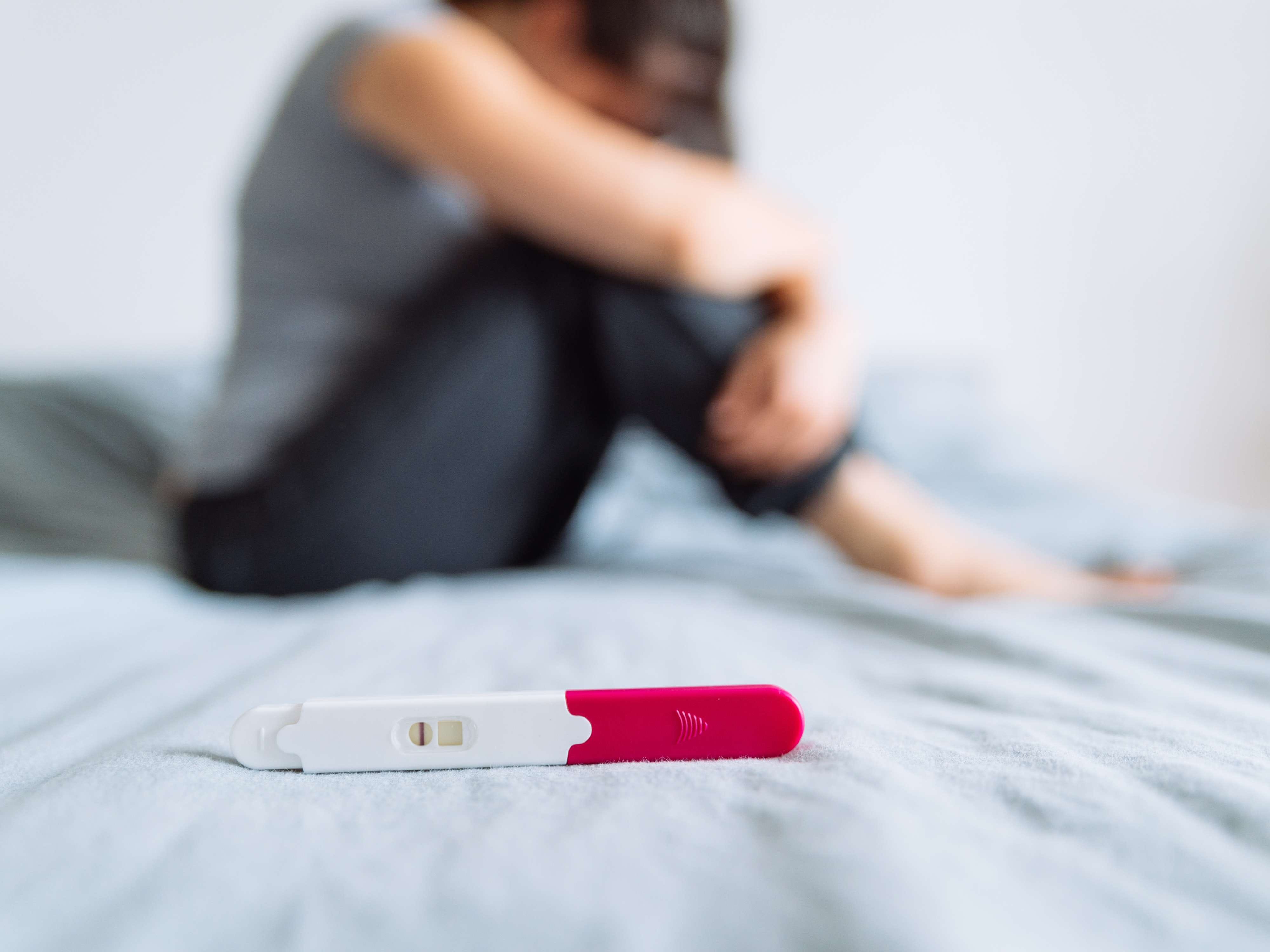 Woman sitting depressed, holding a pregnancy test showing a negative result