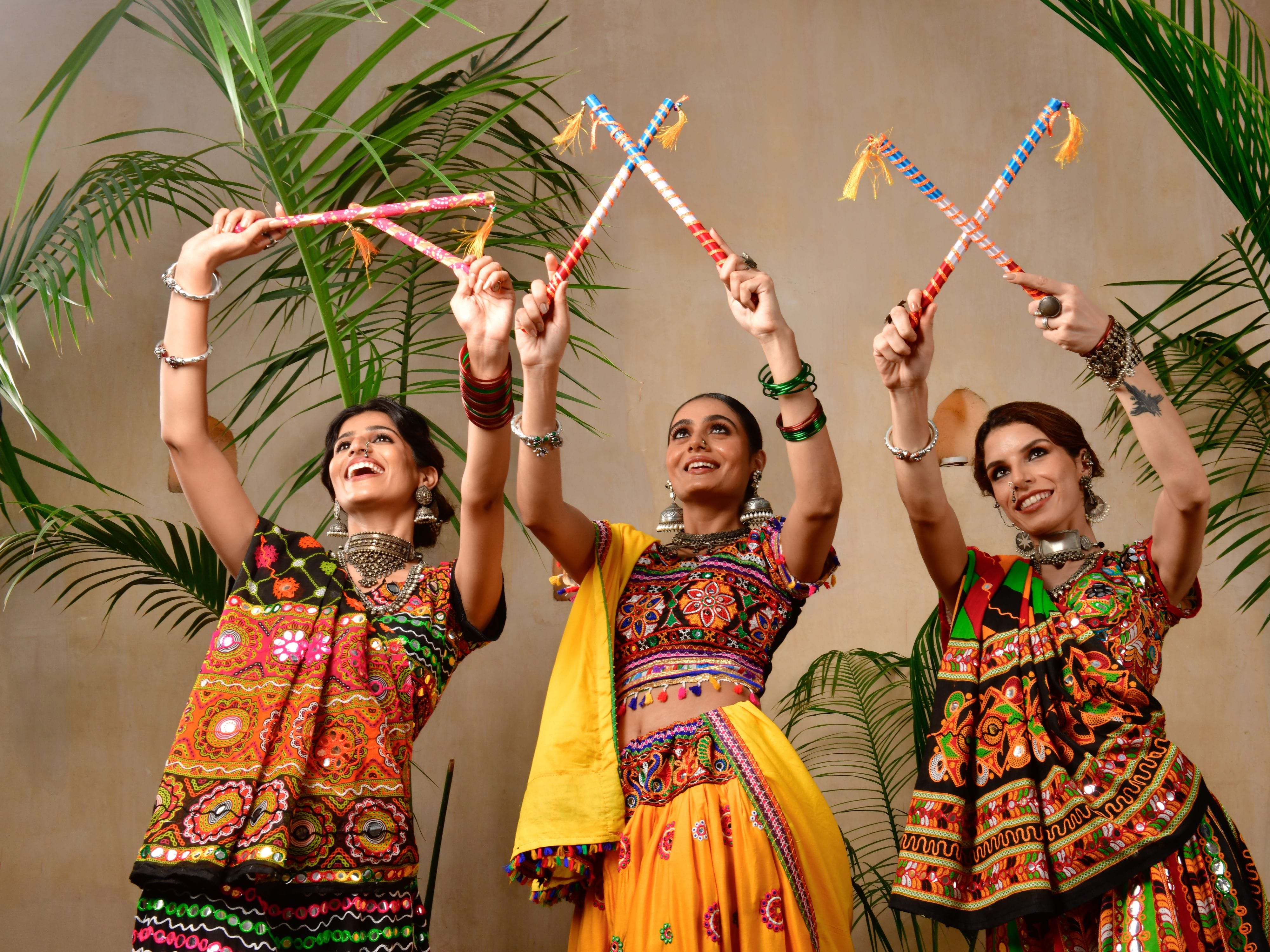 Three women dancing Garba Raas with dandiya sticks