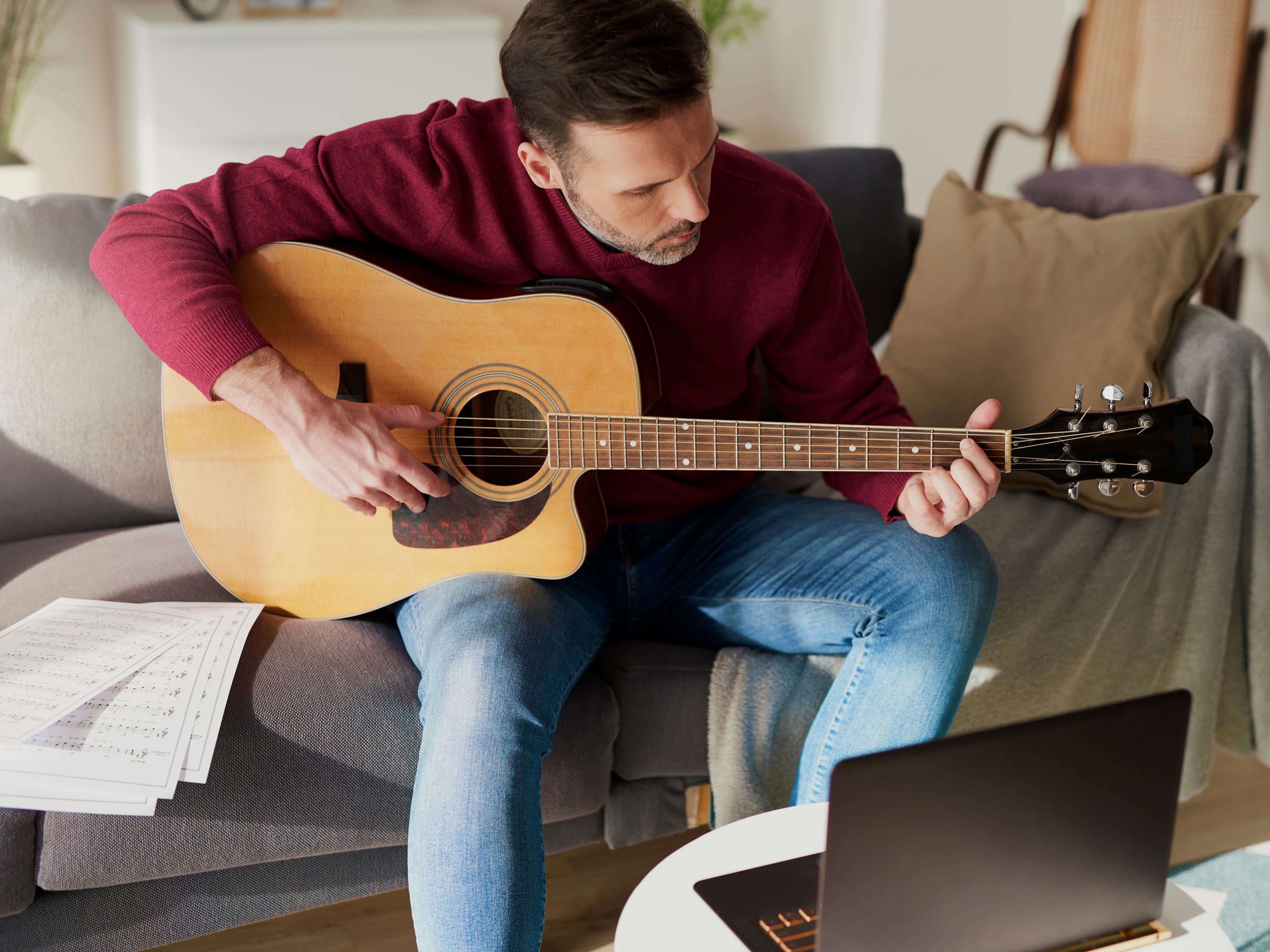 Beginner recording music while playing guitar in front of a laptop