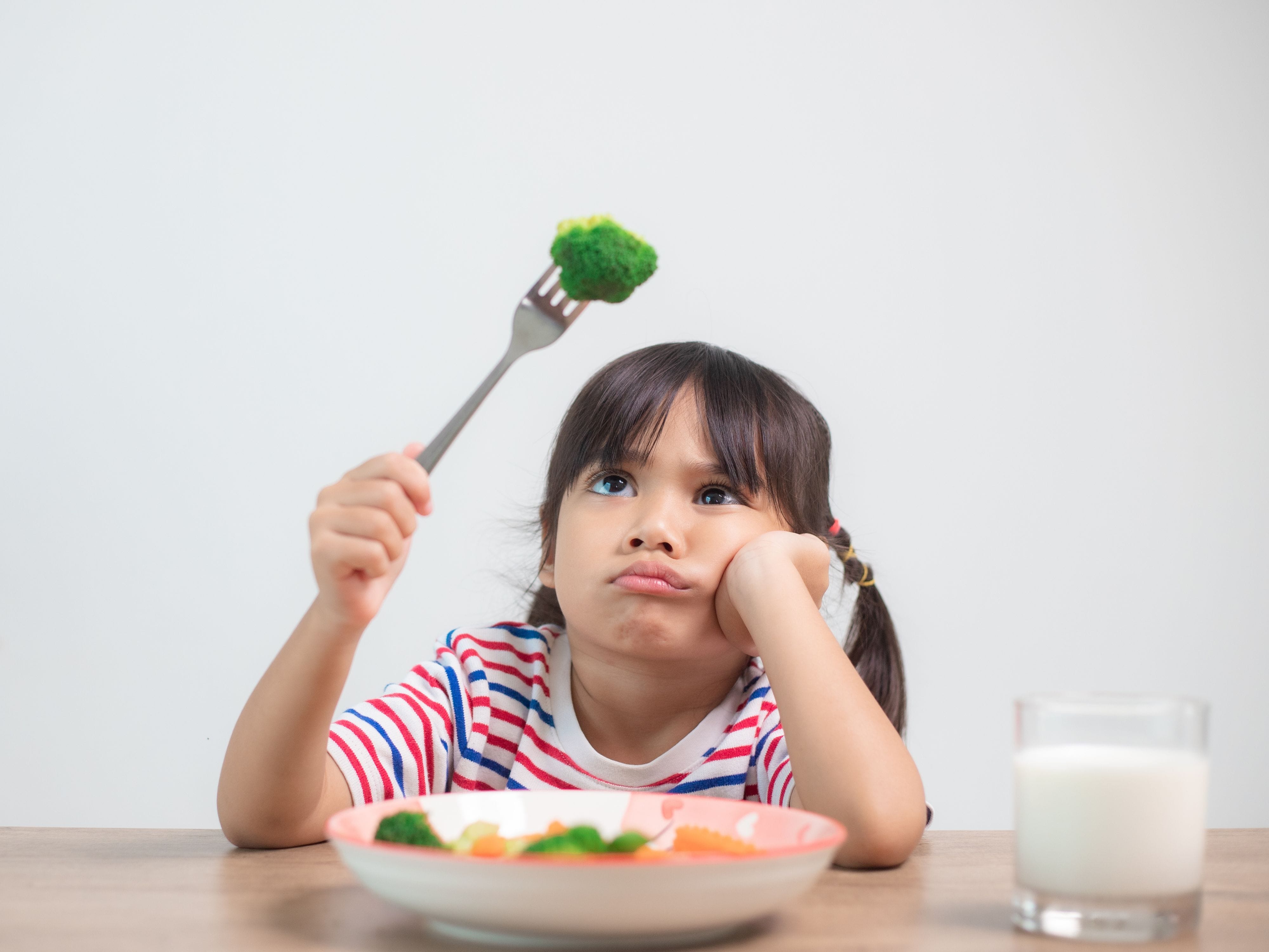 Young girl reluctantly looking at her vegetables, resisting eating healthy