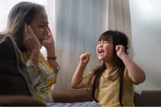 A child yelling at her grandmother while she covers her ears.