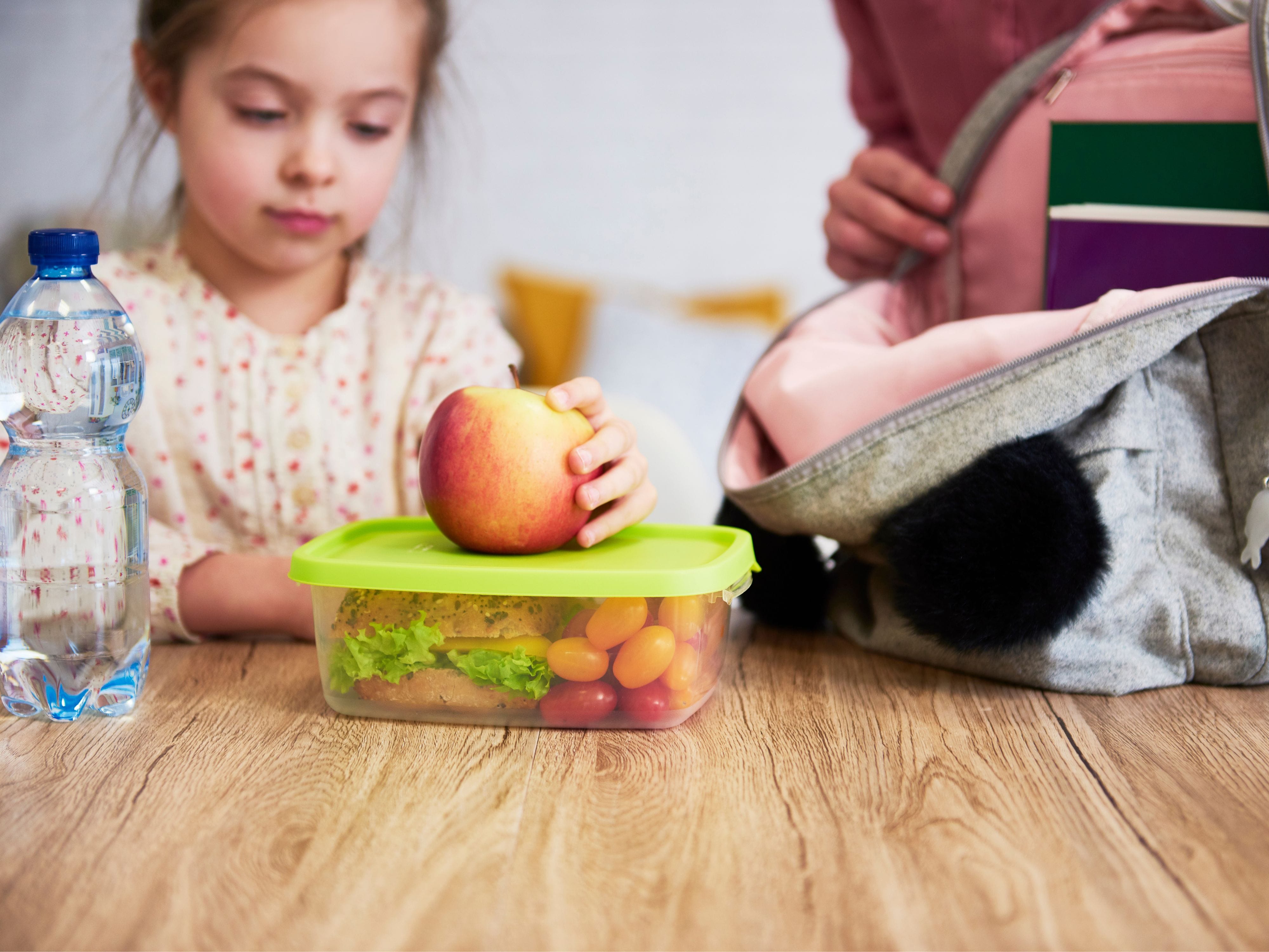 Mother helping her daughter pack her lunchbox filled with fruits and vegetables