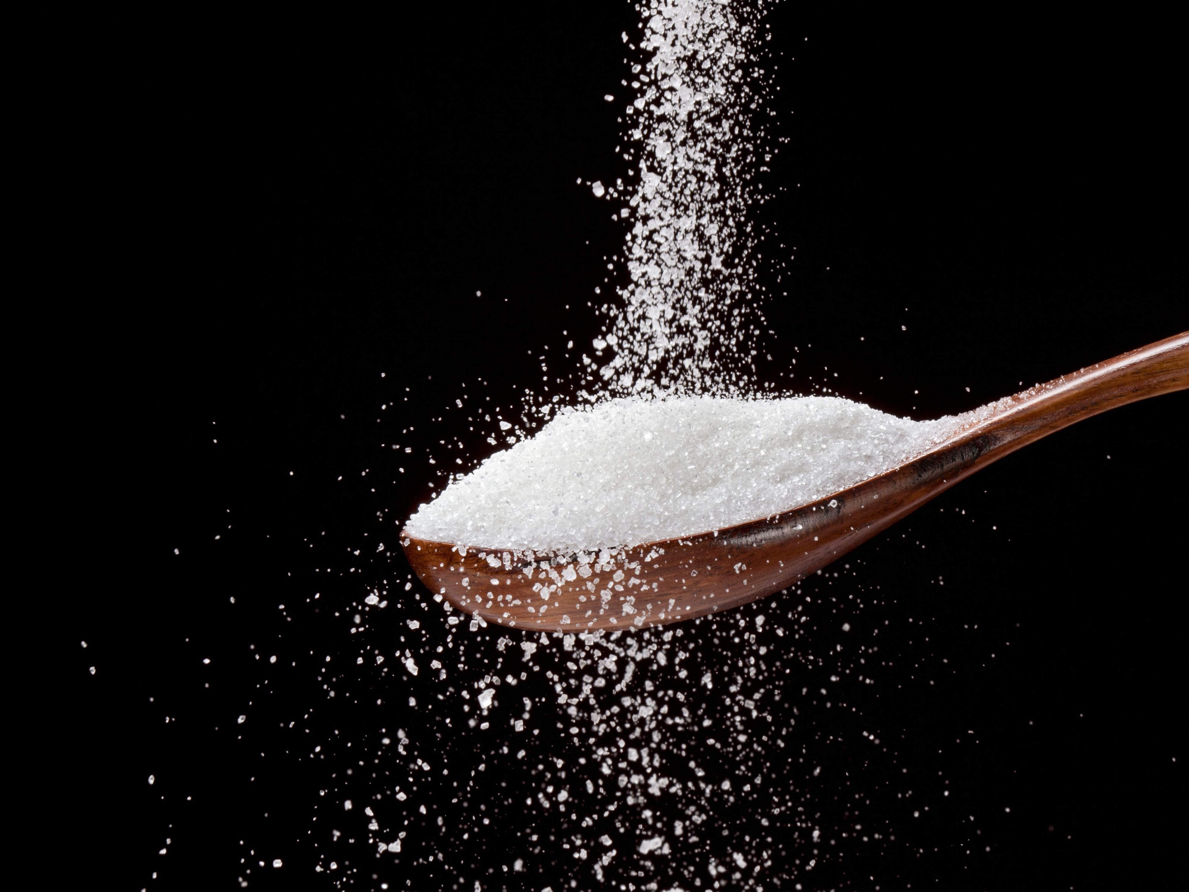 Sugar grains falling onto a wooden spoon filled with sugar