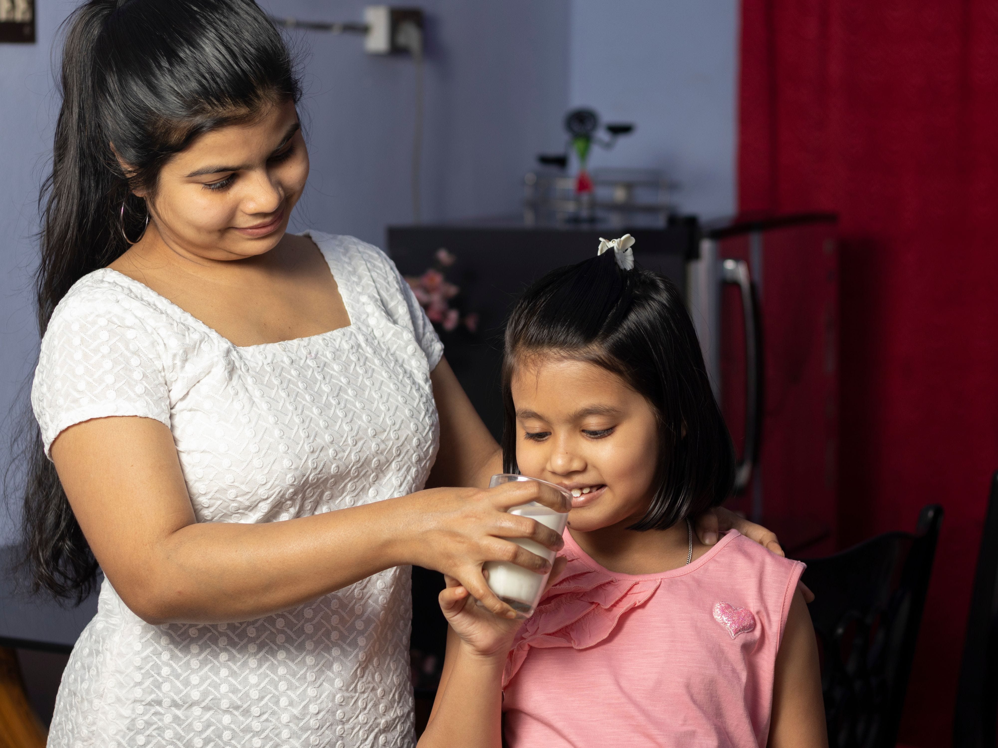 Mother assisting her daughter in drinking a glass of milk