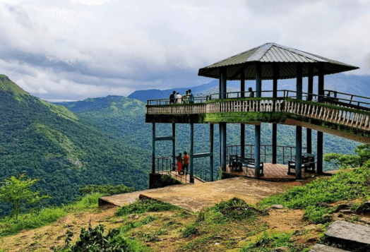 A gazebo viewpoint overlooking the lush green mountain ranges of Sakleshpur, with people enjoying the scenic view