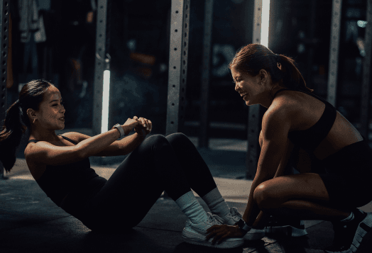 Two women exercising in a gym, one doing situps