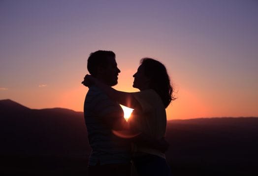 Silhouetted couple embracing against a vibrant sunset and mountains