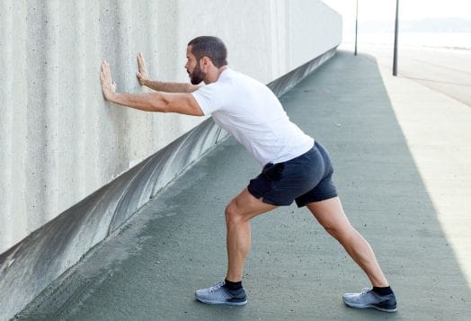 Man stretching calf muscle against a wall