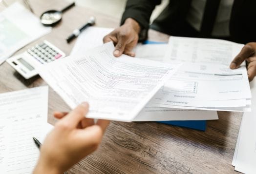 Two people exchanging tax documents across a desk