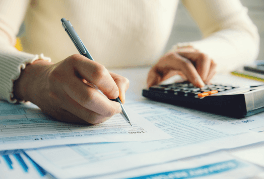 A person's hands filling out tax forms while using a calculator