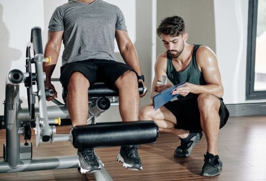 A personal trainer observing a client doing leg extensions at a gym