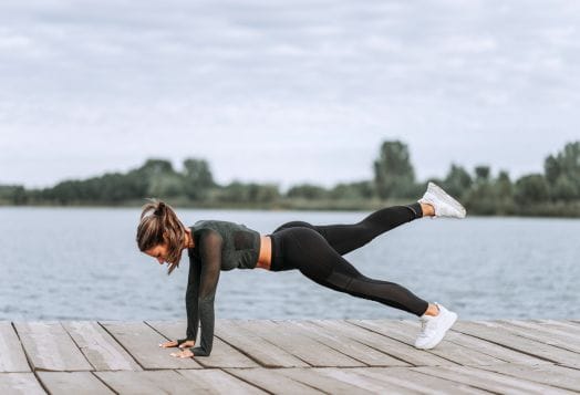 Woman performing plank leg raise on a dock