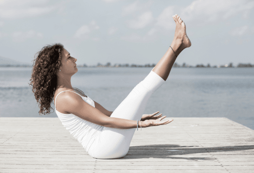 Woman in white, full boat pose by water