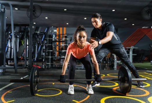 Trainer guiding woman deadlifting at gym