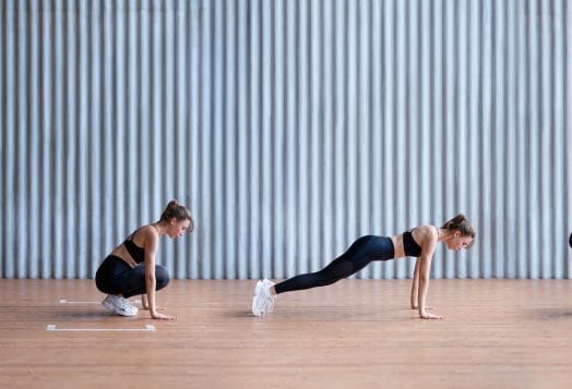 Two women exercising: one squatting, one in plank position indoors