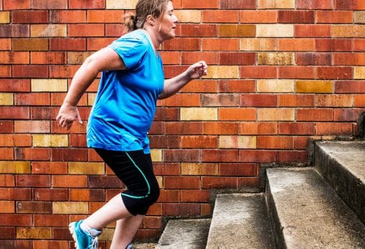 Woman in blue shirt ascending concrete stairs next to brick wall