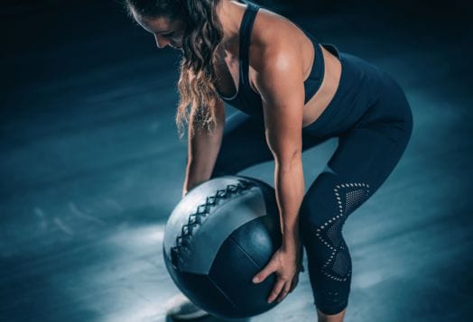 Woman in workout gear gripping a large black and white medicine ball