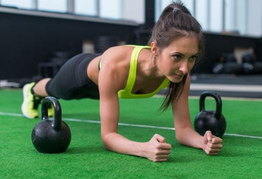 Woman holding a plank pose near kettlebells