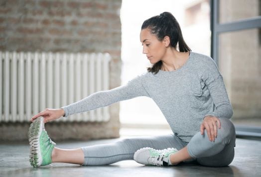 Woman stretching her hamstring, sitting on floor in activewear