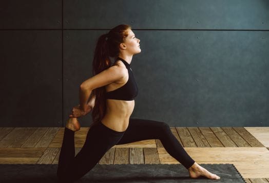 Woman in black activewear performing a quad stretch on a mat