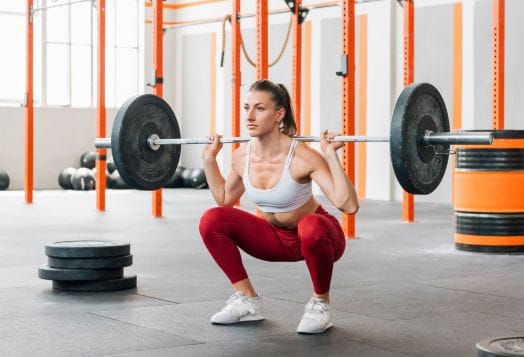 Woman in red leggings doing barbell back squats in a gym