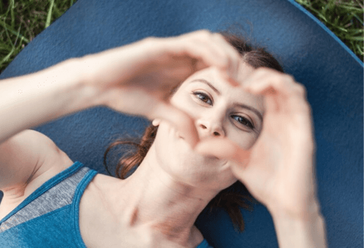 A woman lying on a yoga mat forms a heart shape with her hands