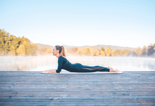 Woman demonstrating Sphinx Pose or Salamba Bhujangasana yoga pose outdoors on a mat