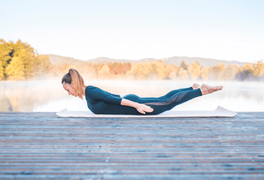 Woman demonstrating Locust Pose or Salabhasana yoga pose on a mat outdoors