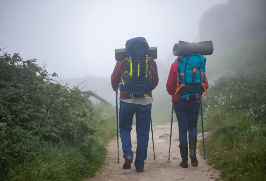Two hikers with backpacks walking on a misty trail