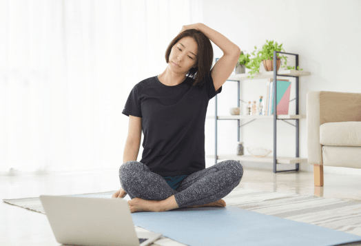 Woman performing a Neck Tilt or Side Bend stretch while sitting on a yoga mat