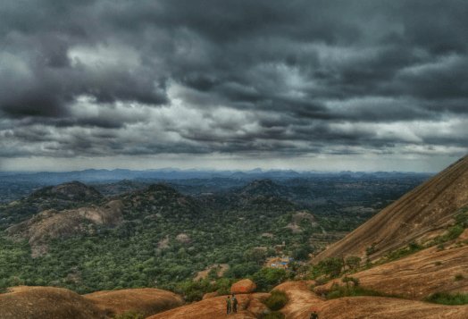 A panoramic view of the rocky hills and lush landscape of Anthar Gange, with a dramatic cloudy sky overhead