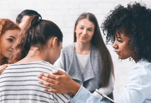 A group of people in a support group, with one person comforting another by placing a hand on their shoulder