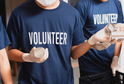 A person wearing a "VOLUNTEER" t-shirt and gloves holds a canned good