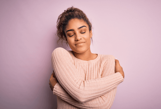 A woman with her eyes closed hugs herself, smiling