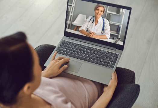A person uses a laptop to have a video call with a smiling doctor
