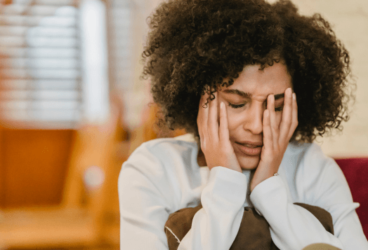 A woman with curly hair looks distressed, holding her face