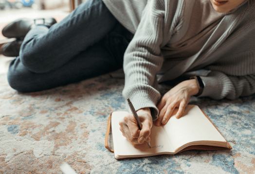 Person lying on floor, writing in an open notebook