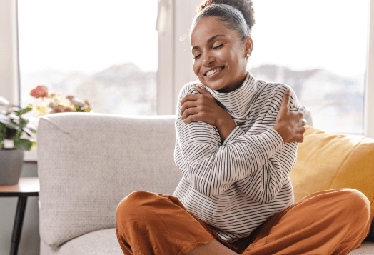 Smiling woman embracing herself on a couch