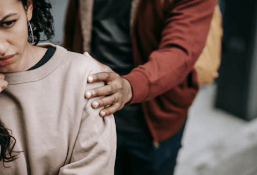 A hand comforting a woman by placing it on her shoulder