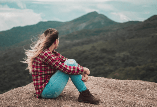 Woman in plaid shirt sitting on mountain, looking at view