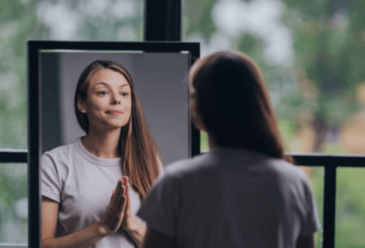 Woman smiling at her reflection in a mirror, hands clasped